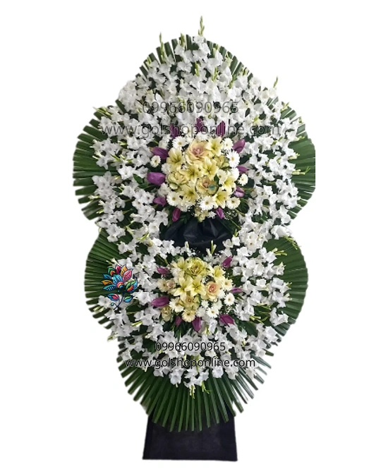 تاج گل زیبا با طراحی خاص، شامل گل‌های سفید، زنبق بنفش و رز کرمی. این تاج گل برای مناسبت‌های مختلف با قیمت مناسب از گل شاپ آنلاین قابل سفارش است.